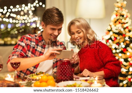holidays, technology and celebration concept - happy couple having christmas dinner at home and photographing food by smartphone