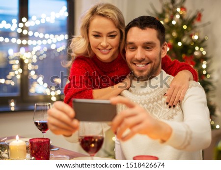 christmas, holidays, technology and people concept - happy couple in taking selfie by smartphone at home dinner