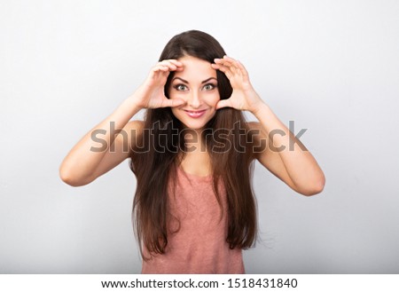 Beautiful funny woman showing the control sign holding hands near the eyes with big eyes on blue background. Binoculars gesture. Closeup
