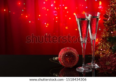 Two champagne glasses and red Christmas ball on a reflective surface on a red background. Christmas bright background. The form is ready to add text or a picture.