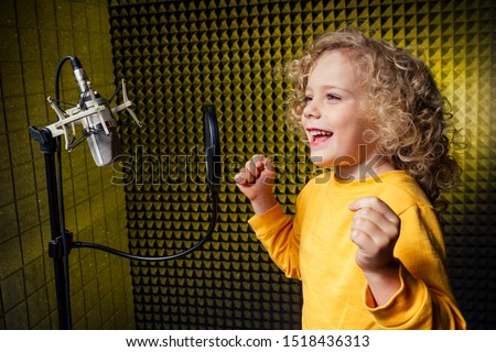 girl blonde curly hair style star singer artist in a yellow blouse with headphone recording new song with microphone.