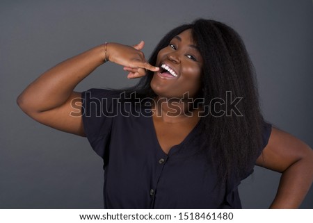 Attractive African American young female in casual clothes imitates telephone conversation, keeps hand near ear as if holding mobile phone, has confident facial expression, isolated outdoors. Call me!