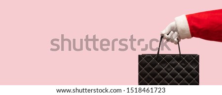 Santa Claus hand holding black leather shopping bag over isolated pink background with clipping path. Black Friday, Sales, Giving Gift for Christmas and New Year 2019.
