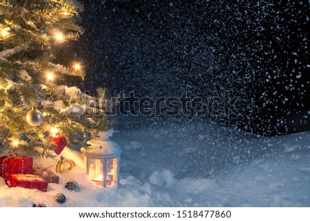 Christmas composition - gifts and a lantern in the snow under a Christmas tree decorated with lights and Christmas-tree decorations, copy space, place for text
