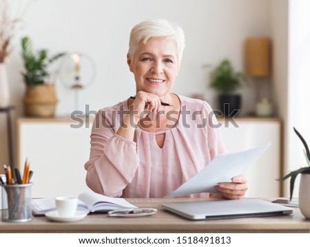 Happy senior business woman working with documents at home, editing text, copy space
