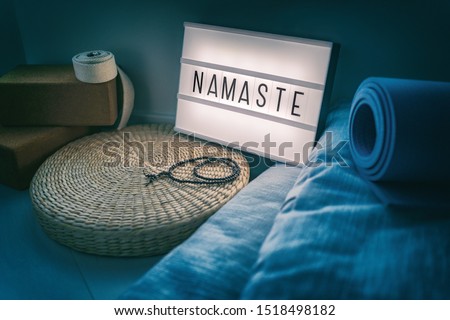 Yoga studio class sign lightbox with letters writing NAMASTE glowing in the night light with natural accessories, rubber mat, cork blocks, organic cotton strap and pillows, straw meditation pillow.