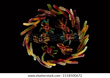 top view of colorful gummy spiders in circle of worms isolated on black, Halloween treat