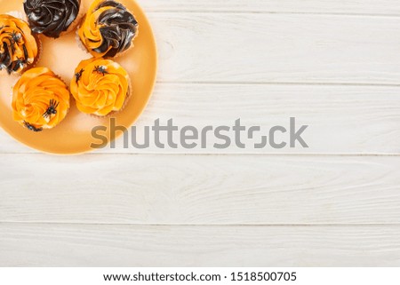 top view of delicious cupcakes with spiders on orange plate on white wooden table, Halloween treat