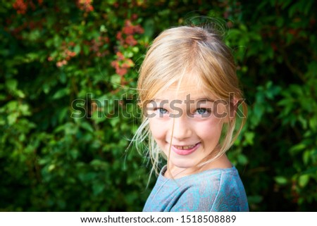 Portrait of cute little child blond girl with blue eyes. Outdoors with greenery background. Selective focus