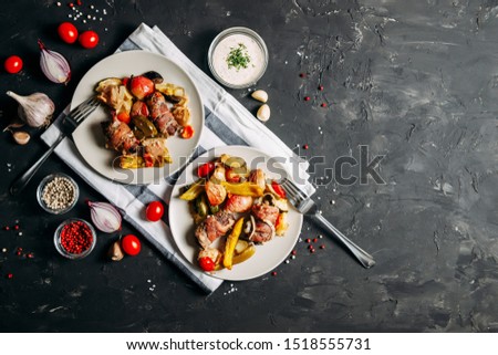 Meat with vegetables on a plate with garlic sauce and spices on a dark wooden background. Baked vegetables (zucchini, peppers, apples, tomatoes) and meat rolls with bacon. Top view. Place for text