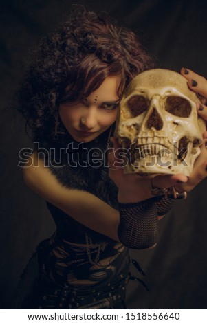 Fashionable kawaii witch with skull posing over dark background. Focus on girl's face not skull.