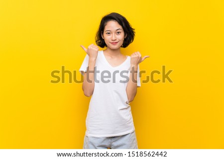 Asian young woman over isolated yellow wall with thumbs up gesture and smiling