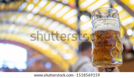 Hand raises a liter beer mug to toast at oktoberfest. Blurred background. Copy space for your text