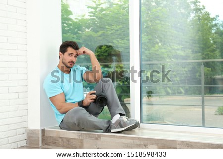 Young photographer with professional camera near window indoors. Space for text