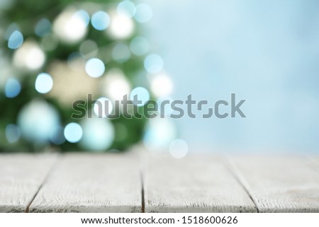 Empty white wooden table and blurred fir tree with Christmas lights on background, bokeh effect. Space for design