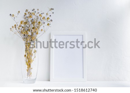 Mockup with a white frame and dry flowers in a vase on a white table