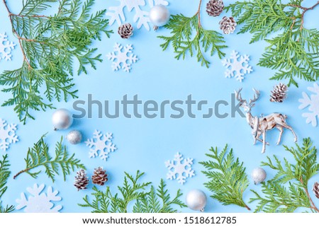 Flat lay christmas frame with snowflakes and evergreen tree branch on a blue background