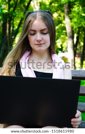 girl with a laptop on a bench in the park on a background of greenery