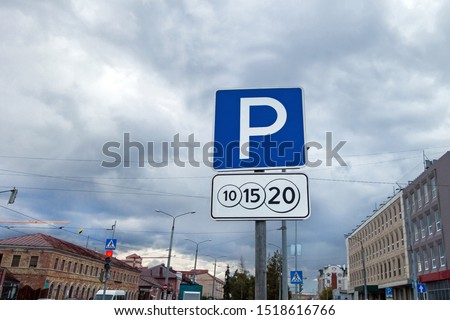 Combination of international traffic signs 'Parking' & 'Payment service'. Urban road traffic & street buildings are on background