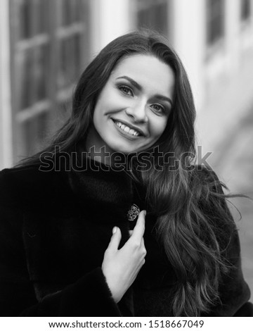 Outdoor portrait of beautiful young pretty woman in black vegan and faux fur coat standing and posing at urban city embankment. Fashion trendy style clothes