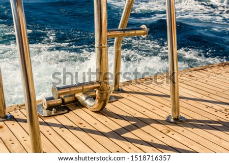 Metal staircase for descent into the water and wave trace with white foam on water surface behind of fast moving yacht
