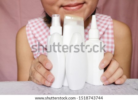 Woman holding different shape of cream and cosmetics white bottle on marble pattern table, person with smile face background