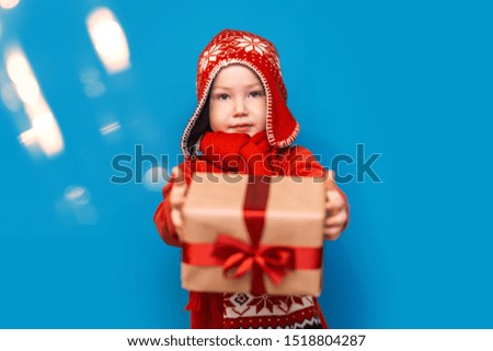 Little baby boy wear santa suit smile and show gift box with red bow on blue background. selected focus. christmas time.
