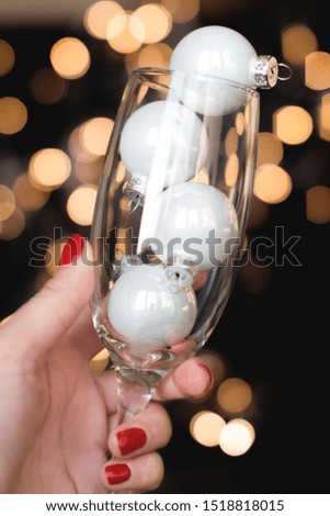 young woman holding a champagne glass with white christmas ornaments on black background with gold christmas lights