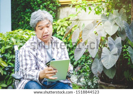 An old man sitting on a wheelchair Hold a tablet and credit card To buy products online. Cerebrovascular disease