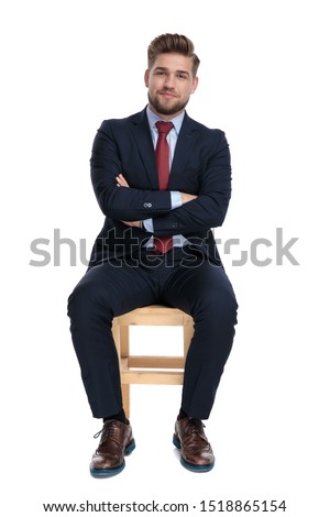 happy young businessman smiling, folding arms and sitting isolated on white background in studio