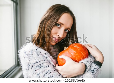 A young woman hugs a pumpkin and smiles