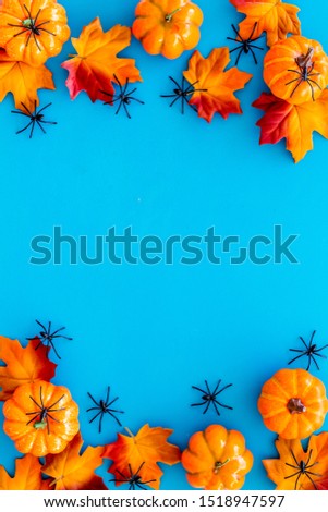 Nice halloween frame. Small spiders among leaves and pumpkins on blue background top view copy space