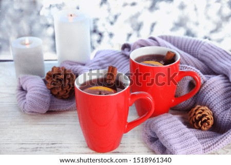 Cups of hot winter drink with knitted sweater on window sill indoors