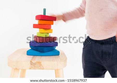 Child playing with a wooden stacking tower painted in Montessori colors, increasing the hight of the tower. Against a white background, showing movement in hands and arms. 