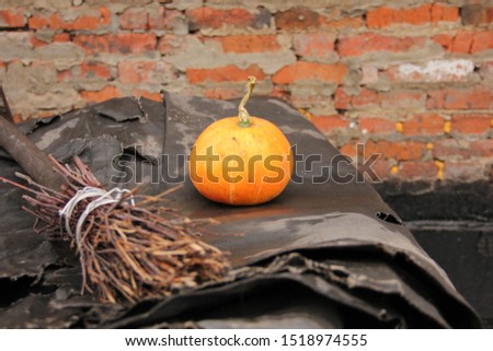 a small orange pumpkin and a broom lie on a black background against a brick wall