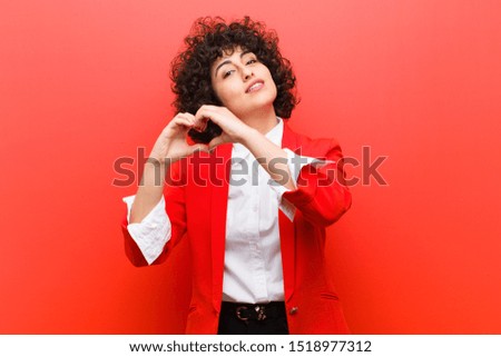 young pretty afro woman smiling and feeling happy, cute, romantic and in love, making heart shape with both hands