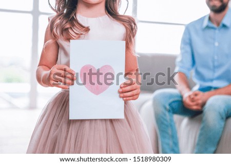 cropped shot of girl holding picture of a heart with father sitting on the couch on the background