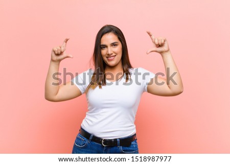 young pretty hispanic woman framing or outlining own smile with both hands, looking positive and happy, wellness concept against pink wall