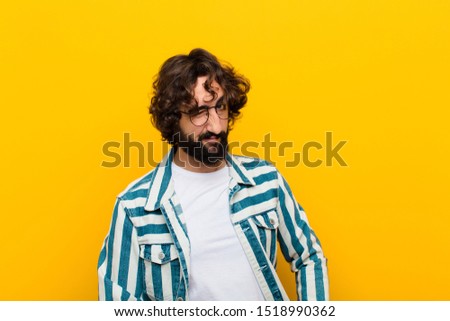 young crazy man looking happy and friendly, smiling and winking an eye at you with a positive attitude against yellow wall