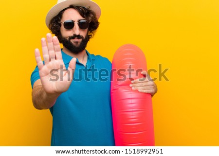 young crazy man looking serious, stern, displeased and angry showing open palm making stop gesture against orange wall