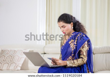 Picture of traditional Indian woman using laptop and credit card while sitting on the sofa at home