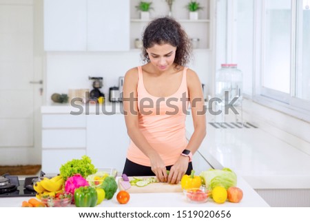 Picture of curly hair woman preparing a healthy salad while standing in the kitchen