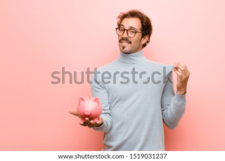 young handsome man with a piggy bank against pink flat wall