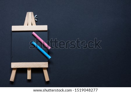 Aerial view of an empty blackboard shaped like an easel on a black background with blue and pink chalk