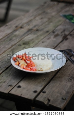 
White rice with side dishes of raw tomatoes and homemade chicken on a wooden table. Low-fat diet. Focus photos on narrow objects and blur backgrounds