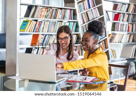 Two business colleagues looking at laptop computer and discussing their startup plan in modern office . African American business woman and her partner sitting at table and talking future deals