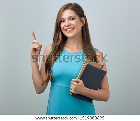 Smiling woman with long hair in blue dress holding books and pointing finger. isolated female portrait.