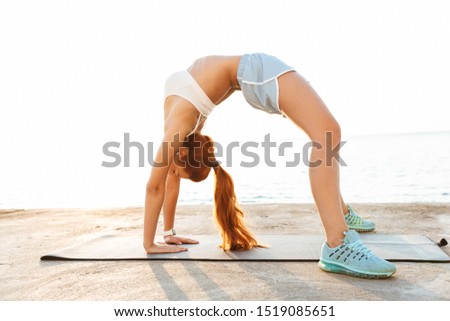 Picture of gorgeous strong amazing beautiful young redhead fitness woman make yoga exercise outdoors at the beach in the morning.