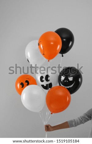 Woman holding color balloons for Halloween party on light grey background, closeup