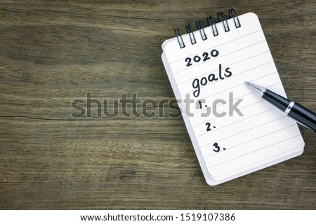 Top view 2020 goals list on notepad. Handwriting on memo paper notebook with black pen over wooden texture background, table blank space. Beginning of new goals and new year resolution concepts. Royalty-Free Stock Photo #1519107386